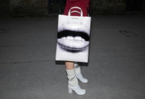 Close-up of a stylish bag with art print, paired with high heels on a nighttime pavement.