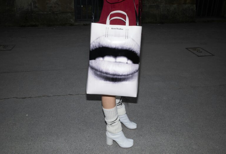 Close-up of a stylish bag with art print, paired with high heels on a nighttime pavement.