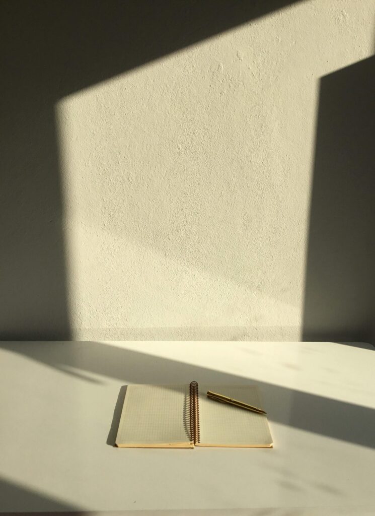 Open notebook and pen on a desk, casting warm shadows, ideal for creative inspiration.