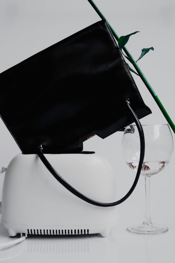 Stylish still life featuring a black handbag, white toaster, and wineglass on a white background.