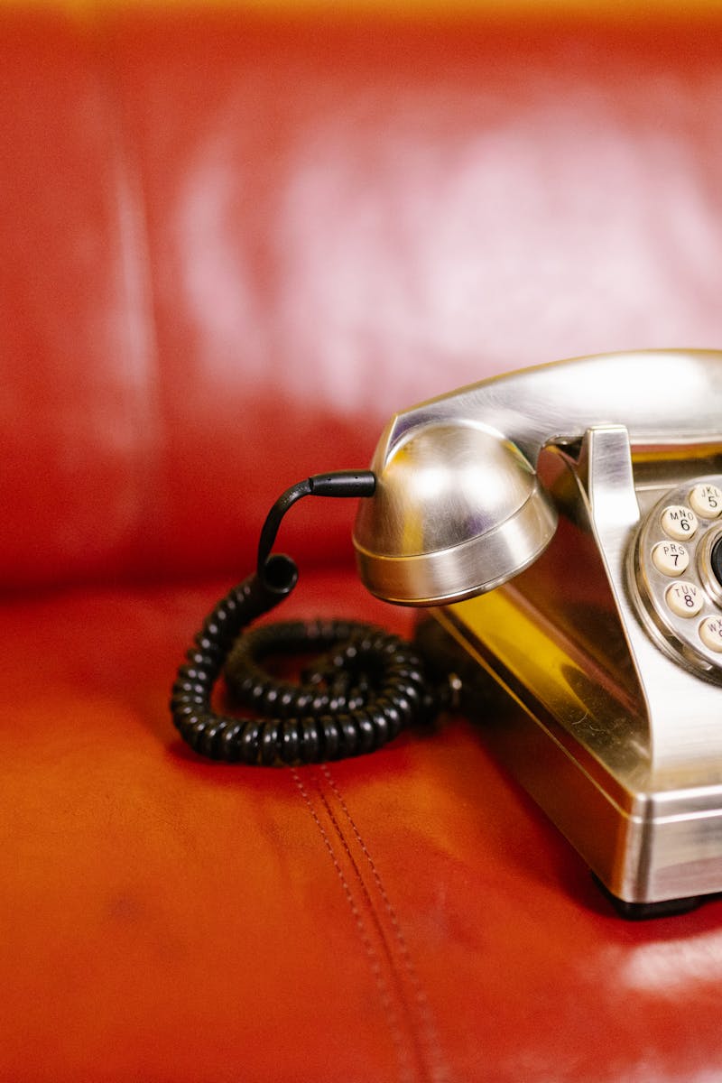 Close-up of a classic rotary phone on a red leather chair, evoking nostalgia.