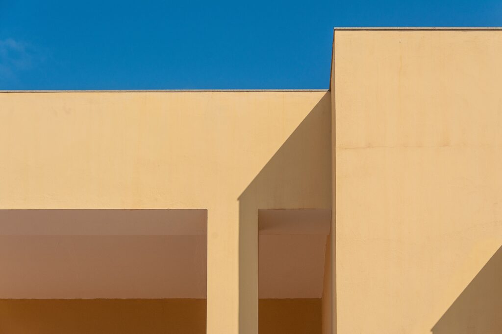 Minimalist architecture with geometric shadows and clear blue sky creates a striking abstract composition.