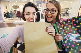 Two women smiling with shopping bags in a mall environment.