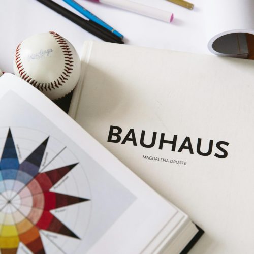 An artistic workspace featuring a Bauhaus design book, art supplies, and a baseball for inspiration.
