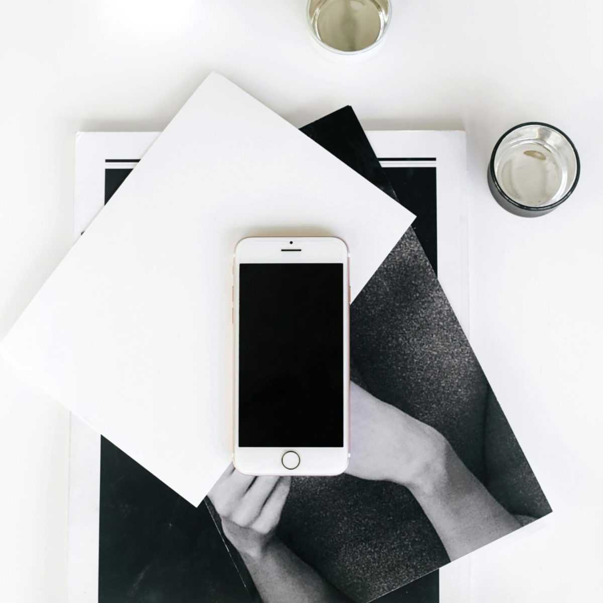 A flat lay photo of a minimalist workspace featuring a smartphone, books, and a vase.