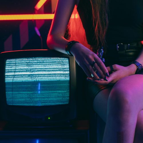 A stylish woman sits in a black skirt with vintage TV static, neon lights creating a moody ambiance.