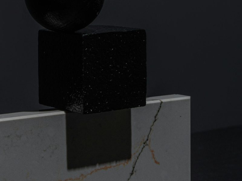 Black geometric sphere and cube on a marble slab, showcasing minimalist design and contrast.